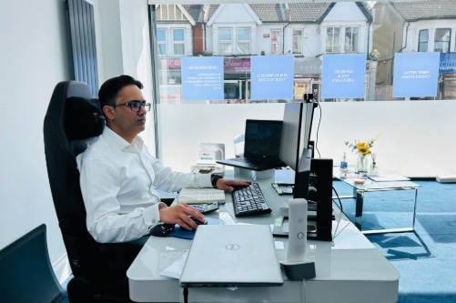 Tax investigation accountant sitting at a desk, focused on his laptop, with a notepad and pen beside him.