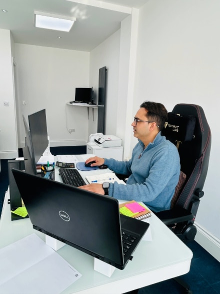 Payroll outsourcing services A man wearing glasses sits at a desk with two computers, focused on payroll outsourcing services.