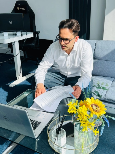 Auto enrolment services Saurabh Bedi glasses sitting on a couch, focused on his laptop while working on auto enrolment services