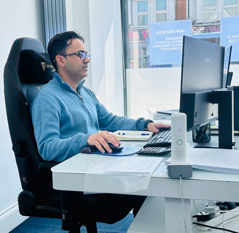 Limited Company Accountant, Saurah Bedin seated at a desk, using a computer and mouse, focused on his work.